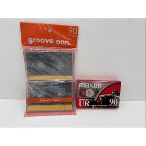 May include: Two cassette tape packs. One orange pack with the text "groove onn." and "90 Minutes" contains two black cassette tapes. A red and black Maxell cassette tape box is also present, labeled "UR" and "90".
