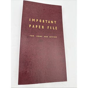 May include: A burgundy paper file with gold lettering that reads "IMPORTANT PAPER FILE" and "FOR HOME AND OFFICE". The file has a textured surface and is rectangular in shape.