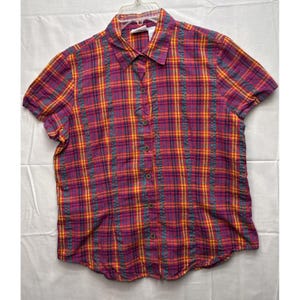 以下が含まれることがあります： 紫、黄色、青の色合いのチェック柄の半袖ボタンダウンシャツ。 シャツには襟があり、前面にボタンが付いています。 生地は軽量に見えます。