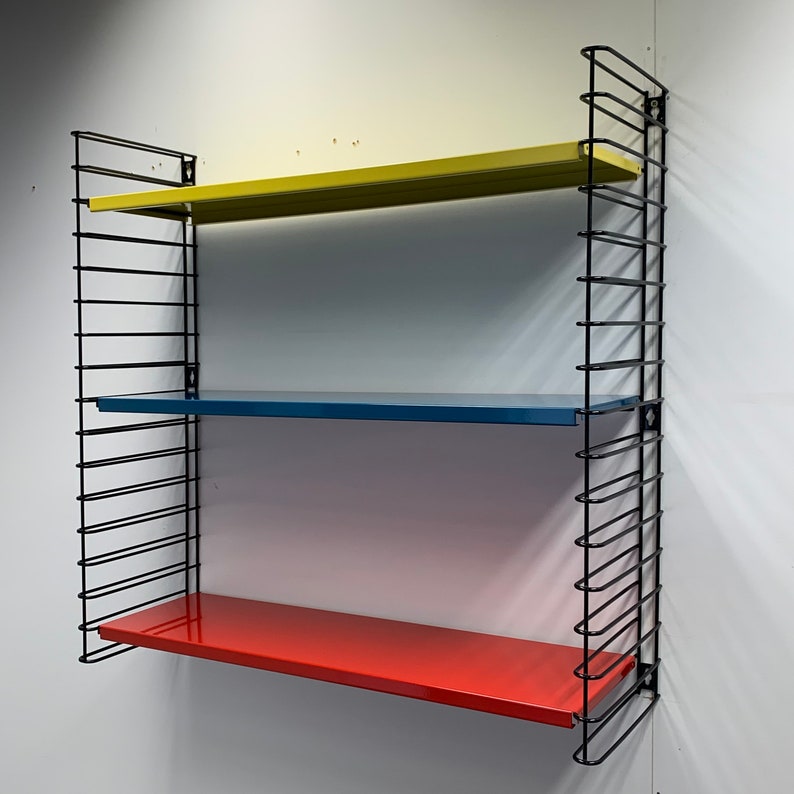 May include: A black metal wall shelf with three shelves. The top shelf is yellow, the middle shelf is blue, and the bottom shelf is red.