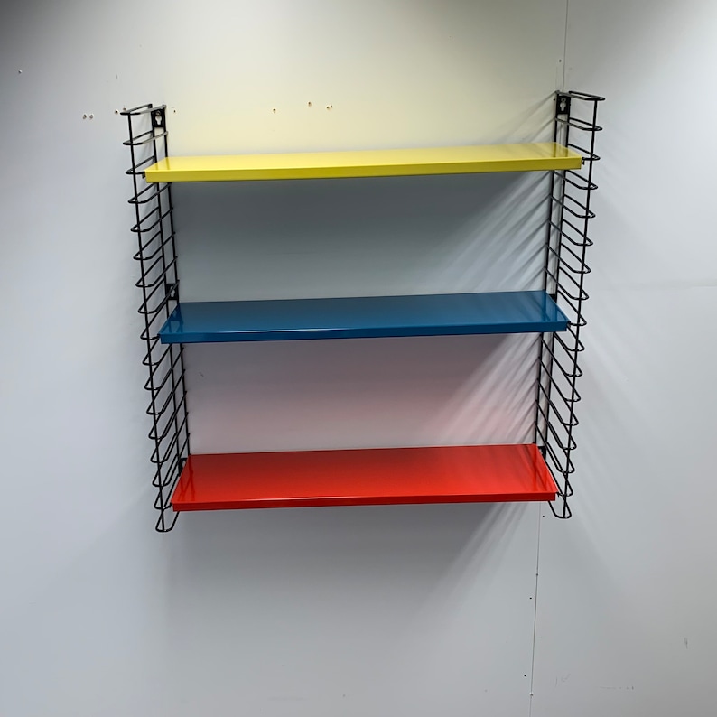 May include: A black metal wall shelf with three shelves. The top shelf is yellow, the middle shelf is blue, and the bottom shelf is red.