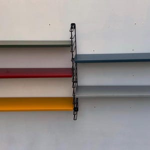 May include: A black metal wall shelf unit with four shelves. The shelves are in different colours: green, red, yellow, and grey.