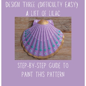 May include: A painted seashell with a lilac and gold design. The shell features a step-by-step guide to paint the pattern. The text on the image reads "Design Three (Difficulty Easy) A Lift of Lilac" and "Step-by-Step Guide to Paint This Pattern."