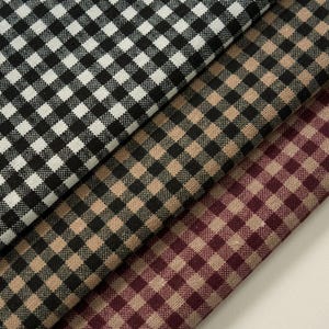 May include: Close-up of three fabric swatches with a classic gingham pattern. The fabrics are in black and white, tan and black, and burgundy and tan. The fabric is folded and layered, showcasing the different colour combinations.