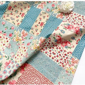 May include: A patchwork quilt with floral and polka dot patterns in cream, light blue, red, and pink. The quilt displays a variety of floral designs and is folded over, showing the fabric's texture and colour variations.