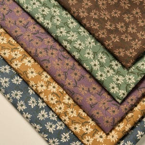 May include: A selection of floral patterned fabric in shades of blue, gold, purple, green, and brown. Each fabric displays a repeating daisy design in white or cream. The fabrics are arranged diagonally, showcasing the different colours and patterns.