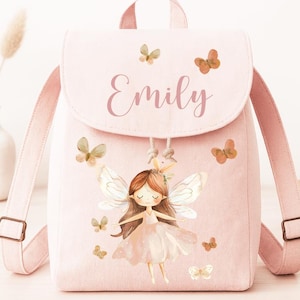 Könnte beinhalten: Ein hellrosa Rucksack mit verstellbaren Trägern und einem oberen Griff. Auf der Klappe steht der Name "Emily" in Schreibschrift und ist mit Schmetterlingen verziert. Die Vorderseite des Rucksacks zeigt eine Illustration einer Fee mit Schmetterlingsflügeln.