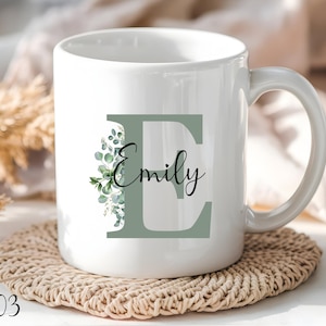 Könnte beinhalten: Weiße Keramiktasse mit einem grünen Blattdesign und dem Buchstaben "E" in hellgrün. Der Name "Emily" ist in schwarzer Schrift unter dem Buchstaben geschrieben.