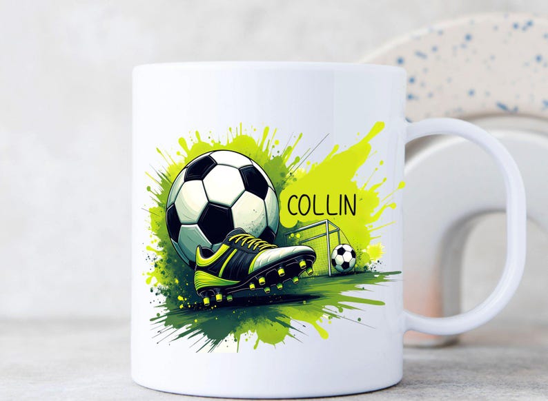 May include: White ceramic mug featuring a soccer ball, cleats, and a small goal, with the name "COLLIN" in green. The design includes green and yellow paint splatters, creating a dynamic sports-themed look.