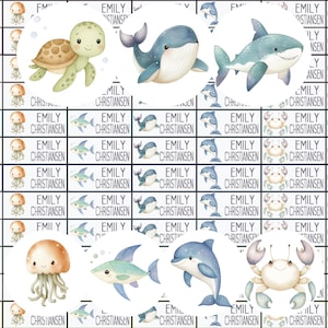 Könnte beinhalten: Eine Sammlung von Aufklebern mit Meerestieren wie Schildkröte, Wal, Hai, Qualle, Fisch, Delfin und Krabbe. Jeder Aufkleber trägt den Namen "EMILY CHRISTIANSEN".
