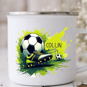 May include: White enamel mug featuring a soccer theme. The design includes a soccer ball, cleats, and a small goal, set against a backdrop of green and yellow paint splatters. The name "COLLIN" is also displayed.