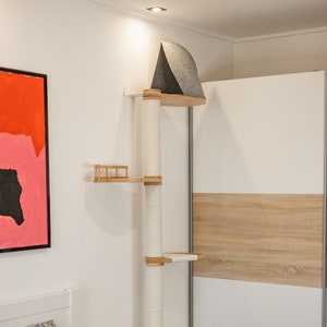 May include: A wall-mounted cat tree featuring a tall central post wrapped in white sisal rope, three light wood platforms, a small wooden railing on the middle level, and a dark grey felt-covered triangular hideaway at the very top.