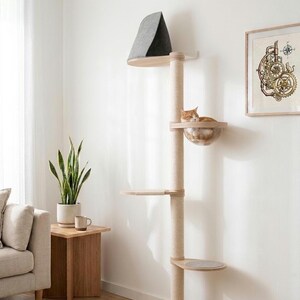 Peut inclure: Un arbre &agrave; chat du sol au plafond avec un poteau central vertical recouvert de corde de sisal claire, plusieurs plateformes en bois, un lit en forme de bol en acrylique transparent contenant un chat orange et un perchoir sup&eacute;rieur en tissu gris fonc&eacute;.