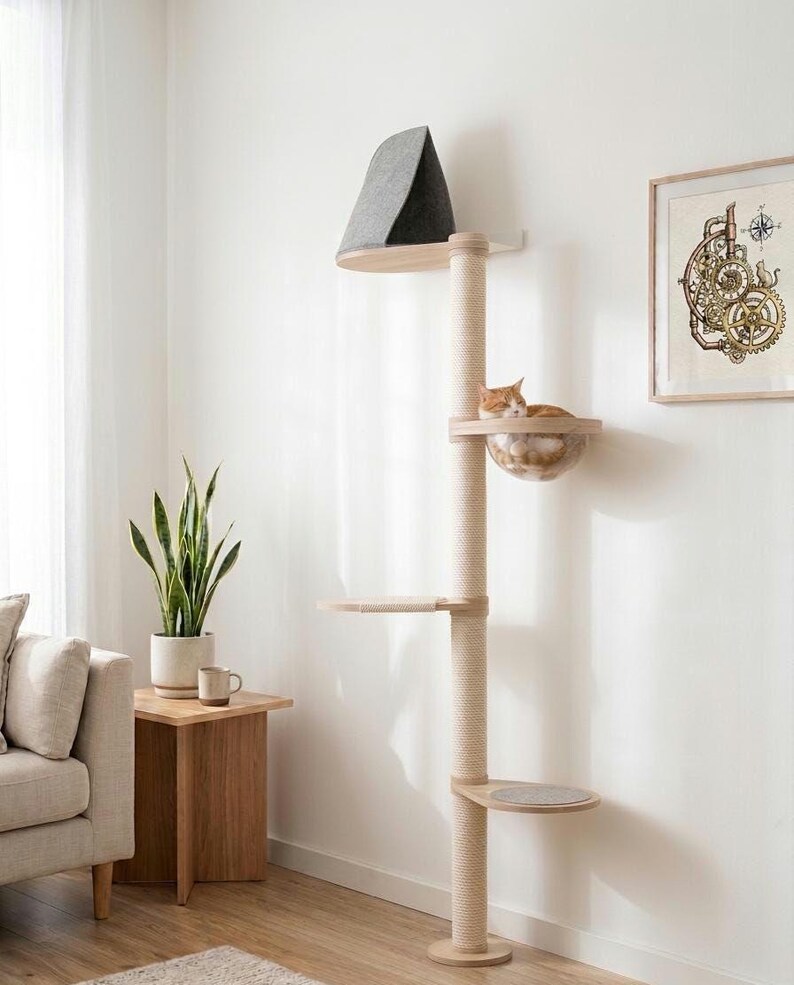 Peut inclure: Un arbre &agrave; chat du sol au plafond avec un poteau central vertical recouvert de corde de sisal claire, plusieurs plateformes en bois, un lit en forme de bol en acrylique transparent contenant un chat orange et un perchoir sup&eacute;rieur en tissu gris fonc&eacute;.