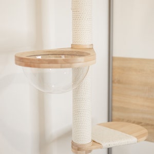 May include: A cat tree post covered in white rope with a wooden platform and a clear plastic bowl. The bowl is attached to the platform with a wooden rim.