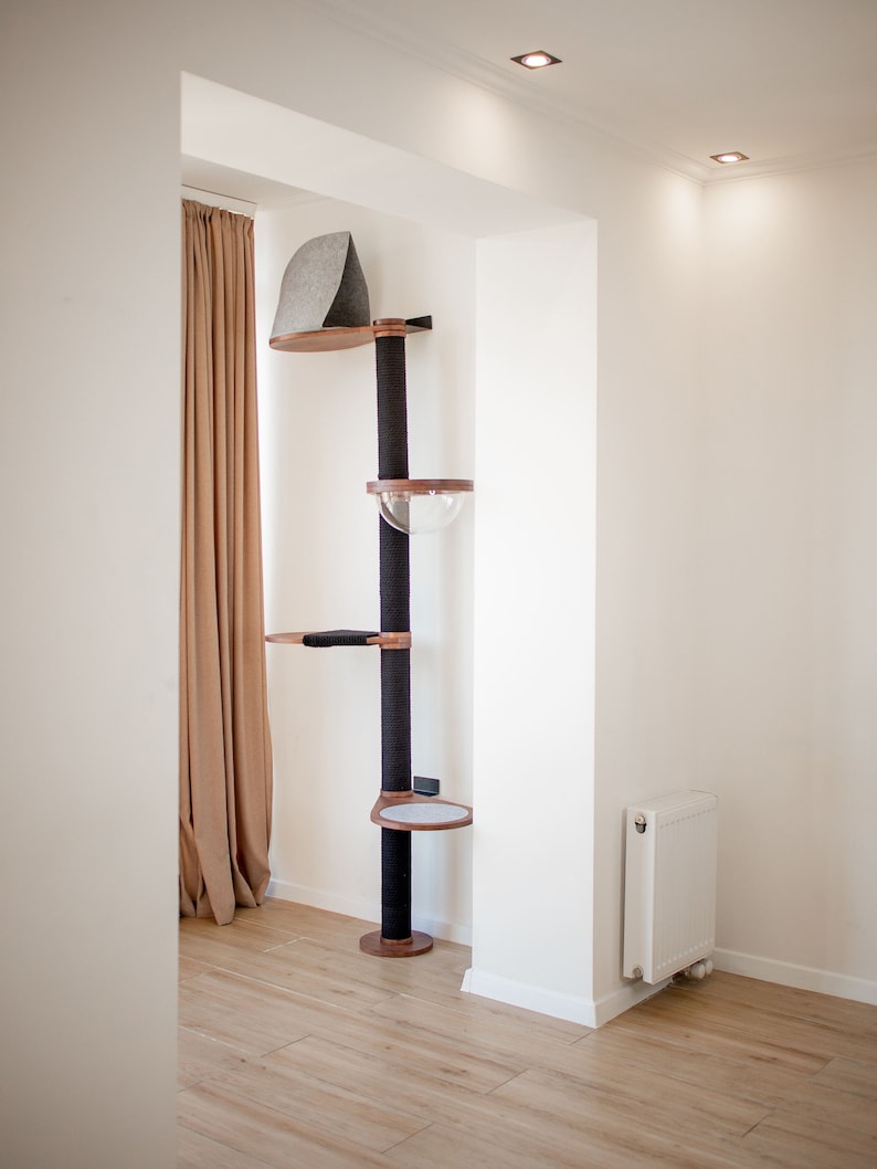 May include: A floor-to-ceiling cat tree featuring a central black sisal-wrapped post, wooden platforms, a clear acrylic dome bed, a gray felt-covered top hideaway, and a small circular platform with a light gray cushion at the base.