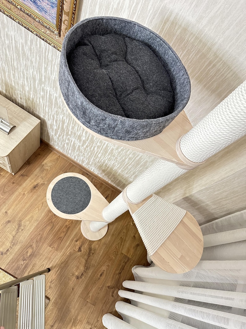 Op de afbeelding: Een kattenboom met meerdere niveaus met een grijs vilten bed, een sisal krabpaal en houten platforms. De kattenmeubels hebben een modern design en zijn gemaakt van lichtgekleurd hout en wit touw.