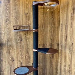 May include: A modern cat tree with multiple levels and features. It has a central black sisal-wrapped post, wooden platforms, and a clear, dome-shaped bed. The tree is designed for climbing and lounging, with a sleek, contemporary aesthetic.