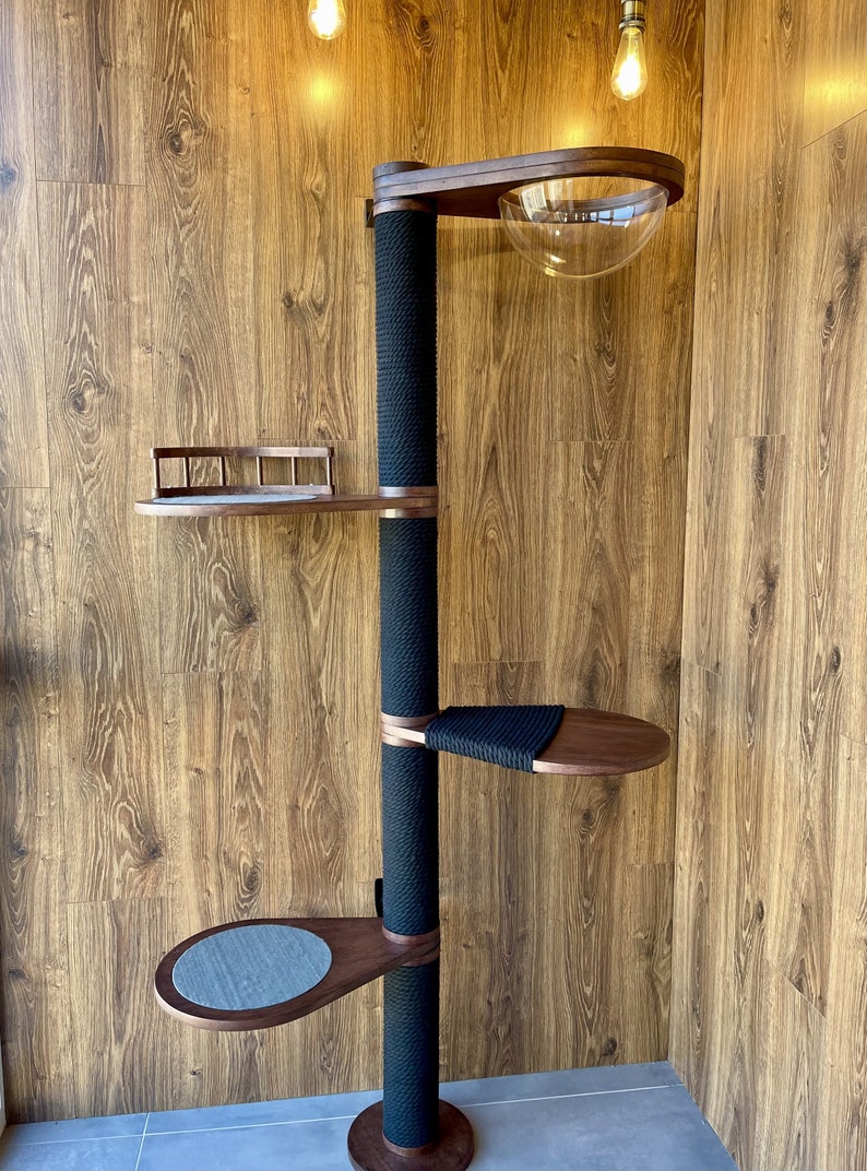 May include: A modern cat tree with multiple levels and features. It has a central black sisal-wrapped post, wooden platforms, and a clear, dome-shaped bed. The tree is designed for climbing and lounging, with a sleek, contemporary aesthetic.