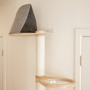 May include: A wall-mounted cat tree featuring a vertical post wrapped in white sisal rope, a top platform with a gray felt triangular enclosure, and a lower wooden platform containing a clear, hemispherical acrylic bowl for resting.