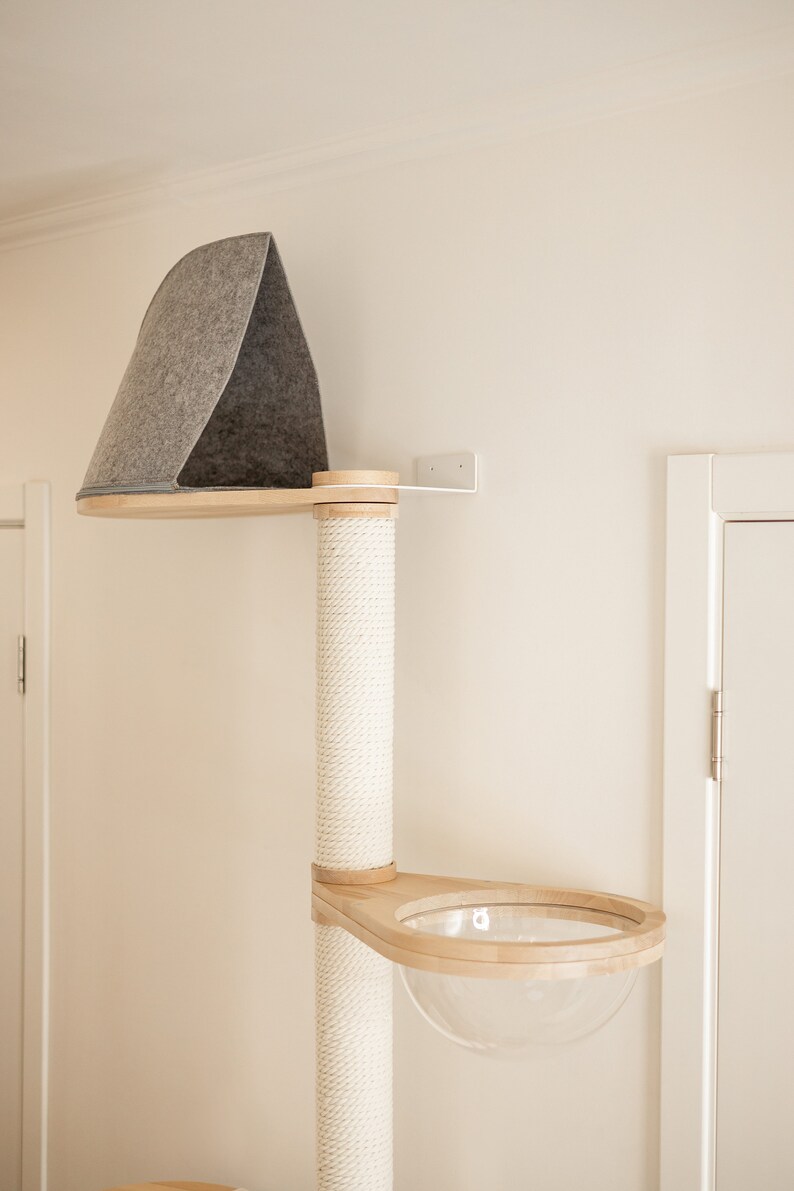May include: A wall-mounted cat tree featuring a vertical post wrapped in white sisal rope, a top platform with a gray felt triangular enclosure, and a lower wooden platform containing a clear, hemispherical acrylic bowl for resting.