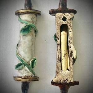 Puede incluir: Dos soportes de rollo de cerámica, uno con un rollo dentro y el otro con un diseño de vid. El soporte de rollo con el diseño de vid tiene un borde dorado.