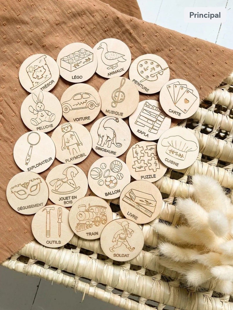 May include: A set of 20 wooden circles with various images and French words on them. The images include a toy car, a dinosaur, a chef, a train, a soldier, a book, a ball, a puzzle, a rocking horse, a magnifying glass, a mask, a set of tools, a Lego brick, a stuffed animal, a musical note, a paint palette, a deck of cards, a stack of wooden blocks, and a duck. The words on the circles are "Tresor", "Lego", "Animaux", "Peluche", "Voiture", "Explorateur", "Deguisement", "Playmobil", "Peinture", "Carte", "Musique", "Kapla", "Dinosaure", "Jouet en Bois", "Ballon", "Puzzle", "Outils", "Train", "Livre", "Soldat", and "Cuisine".