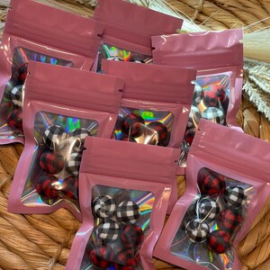 May include: Multiple small pink zippered pouches with clear windows, each containing six red and white plaid fabric balls.