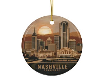 May include: A round ceramic ornament featuring the Nashville, Tennessee skyline at sunset. The ornament has a gold string for hanging. The city's name and state are printed in a dark font at the bottom of the ornament.