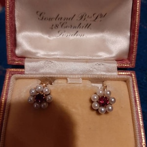 May include: A pair of pearl and ruby earrings in a pink velvet jewelry box. The box is labeled "Gowland Bros Ltd 48 Cornhill London."
