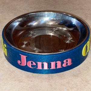 May include: A blue and yellow personalized pet bowl with the name "Jenna" printed in pink.