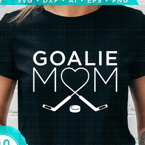Puede incluir: Una camiseta negra con un dise&ntilde;o blanco que dice "Goalie Mom" con un coraz&oacute;n y palos de hockey. El texto "Hand lettered/Hand drawn" est&aacute; en la parte inferior del dise&ntilde;o.
