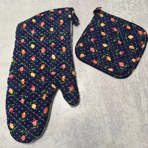 May include: A navy blue quilted oven mitt and matching pot holder. The set features a floral pattern of pink, yellow, and orange tulips with yellow polka dots. The mitt has a loop for hanging.