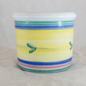May include: A white ceramic planter with a yellow, blue, green and pink striped design. The planter has a green leaf design on the yellow band.
