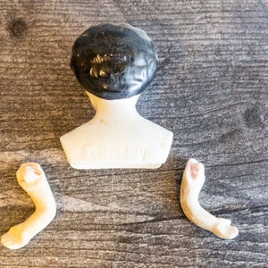 以下が含まれることがあります： 黒い髪の毛と白い胴体を持つ磁器製のドールヘッド。ドールヘッドには「Germany」の刻印があります。磁器製のドールアーム2本も含まれています。