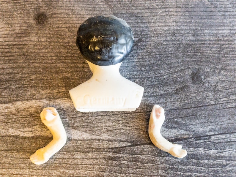 以下が含まれることがあります： 黒い髪の毛と白い胴体を持つ磁器製のドールヘッド。ドールヘッドには「Germany」の刻印があります。磁器製のドールアーム2本も含まれています。