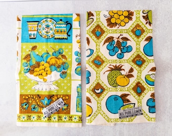 May include: Two vintage linen kitchen towels with fruit and kitchenware designs. One towel features a bowl of fruit, the other has a repeating pattern of fruit. Both towels have the text "ALL PURE LINEN".