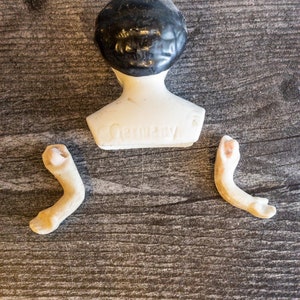 以下が含まれることがあります： 黒い髪の白い陶器のドールヘッドと、白い陶器の胴体。胴体には「Germany」と刻印されています。陶器の腕が2本付属しています。