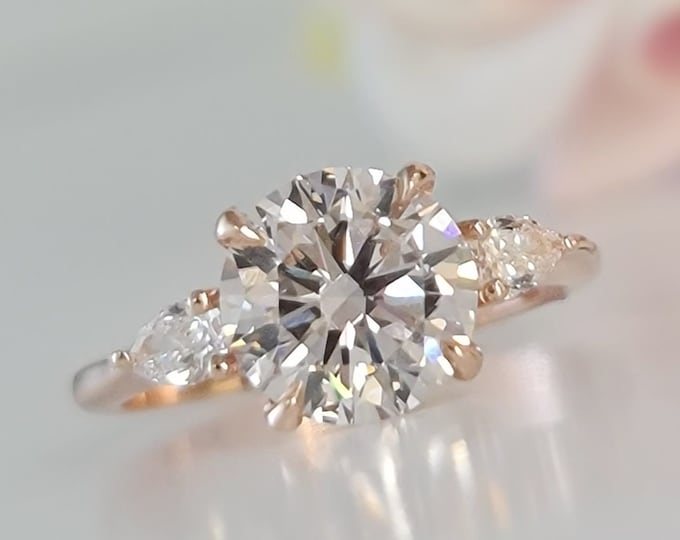 This Classic 14K Rose gold Three Stone Engagement Ring features a 2 carat Ideal round cut diamond and 0.20 carats teardrop side diamonds