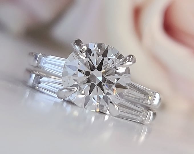 This classic timeless three Stone Diamond Ring features a 2.5 Carat Ideal Round Brilliant Cut IGI Certified CVD lab grown diamond accentuated with 0.50ct tapered baguette side stones accompanied by a 0.70 carats baguette flushing matching wedding band