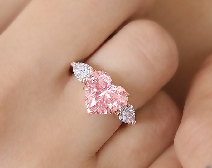 This unique Trilogy Ring features a 3 Carat Pink Heart shape IGI Certified CVD lab grown diamond and 0.70 carats pear cut side diamonds