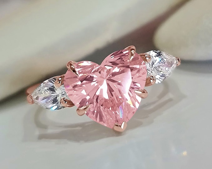 This unique Trilogy Ring features a 3 Carat Pink Heart shape IGI Certified CVD lab grown diamond and 0.70 carats pear cut side diamonds