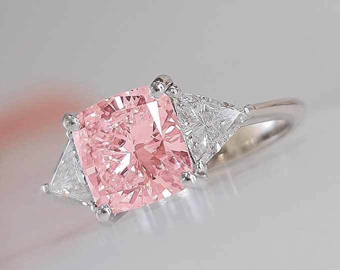 This Unique Three Stone Engagement Ring features a  3.5 Carat IGI Certified CVD lab grown Pink Cushion Cut diamond accompanied by 0.70 carats triangle cut side diamonds