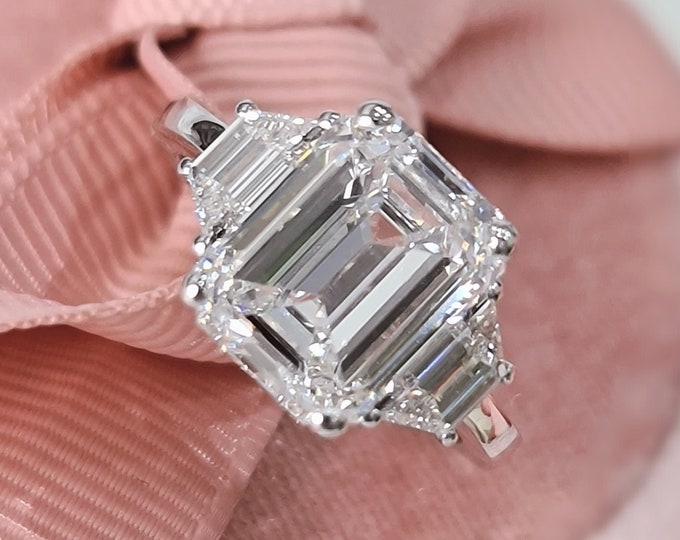 This Unique 14K white gold three Stone Ring features a 4 carat emerald cut IGI Certified CVD lab grown diamond accentuated with 0.70ct step cut trapezoid cut side stones