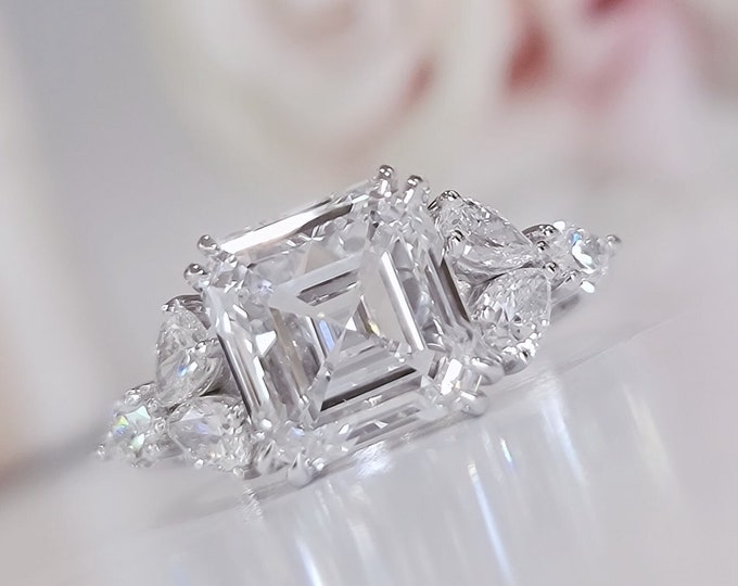 This timeless classic 3 stone ring features a 5 Carat Asscher Cut IGI certified CVD lab grown Diamond and 0.96 carats teardrop side stones