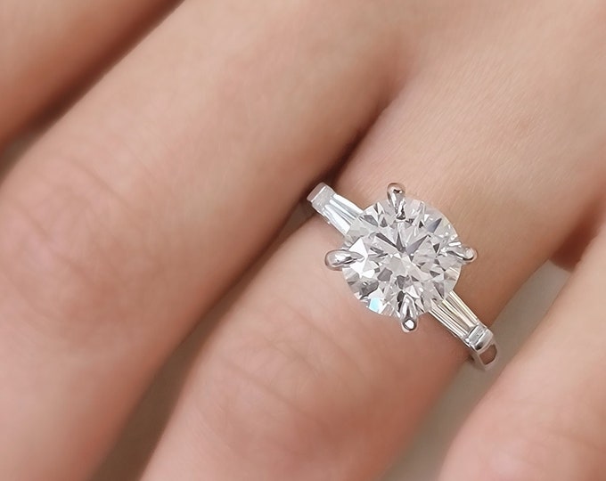 This classic timeless three Stone Diamond Ring features a 3 Carat Ideal Round Brilliant Cut IGI Certified CVD lab grown diamond accentuated with 0.50ct tapered baguette side stones