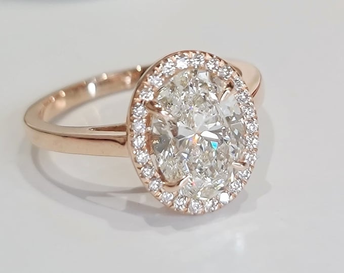 This unique 14K rose gold diamond halo ring features a 2.50 carat oval cut IGI certified CVD lab grown diamond accentuated with 0.13 carats round brilliant diamonds