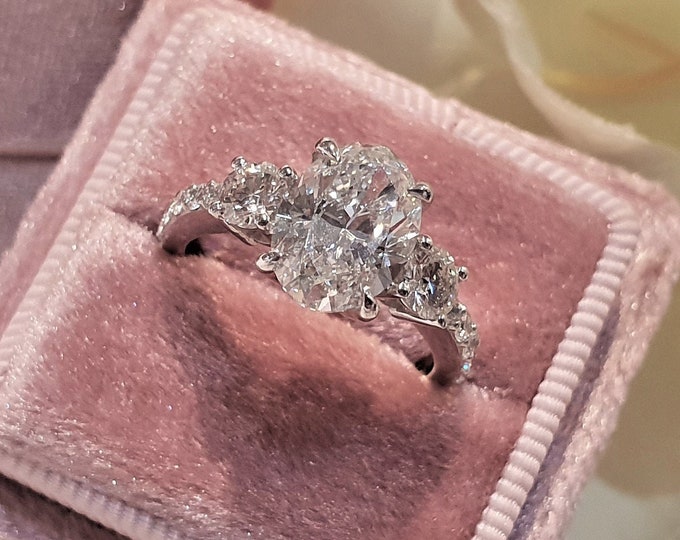 This Unique Three Stone Ring features a 2 Carat Oval Cut IGI Certified CVD lab grown diamond accentuated with 0.40ct round cut side stones and diamond pave setting