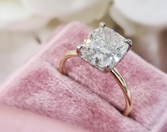 This dainty 2 tone 14K gold hidden halo setting features a 2.50 carat cushion cut IGI certified CVD lab grown diamond & 0.19cts accent diamonds