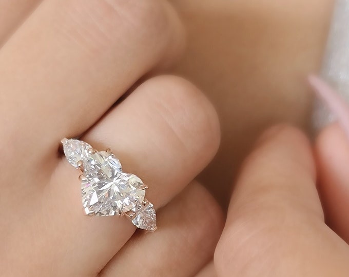 This Unique Rose Gold Three Stone Ring features a 3  Carat Heart Shaped IGI Certified CVD lab grown diamond accentuated with 0.70ct teardrop diamond side stones